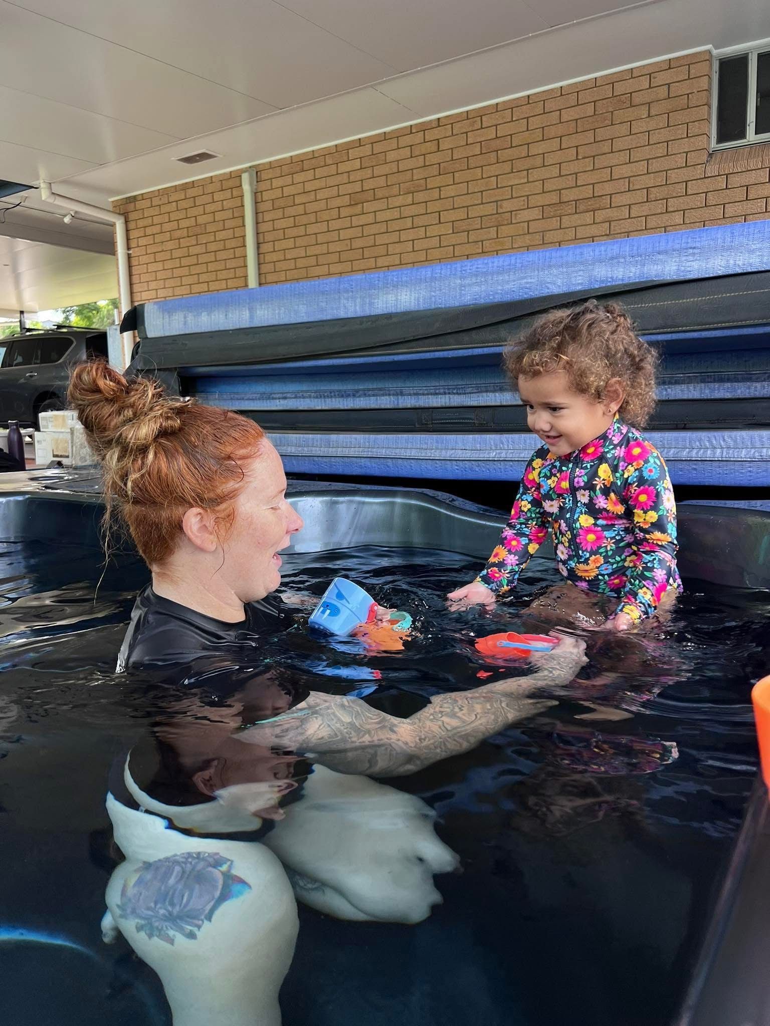 A Woman is Holding a Baby in a Swimming Pool — Earth Angels Child Care Centre in Tinonee, NSW
