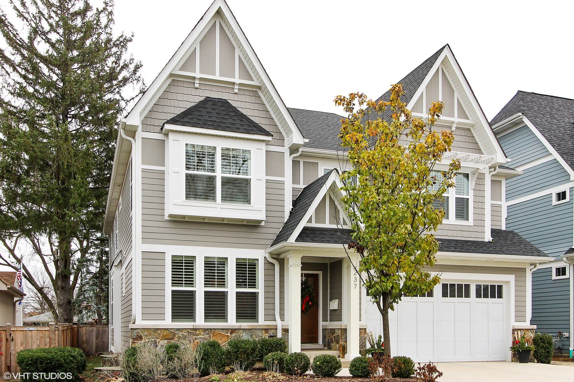 A large house with a white garage door and a tree in front of it.