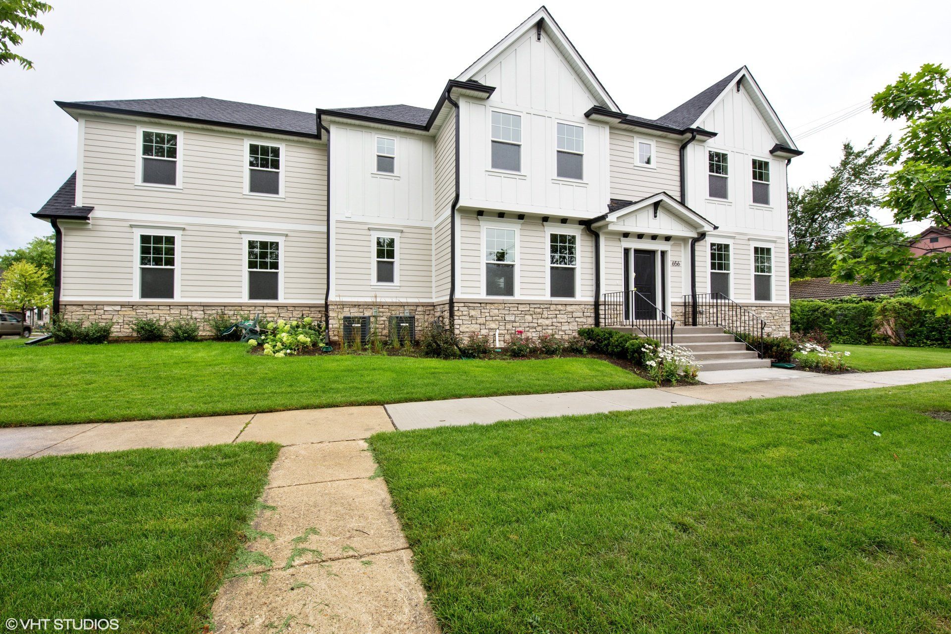 A large white house with a black roof is sitting on top of a lush green lawn.