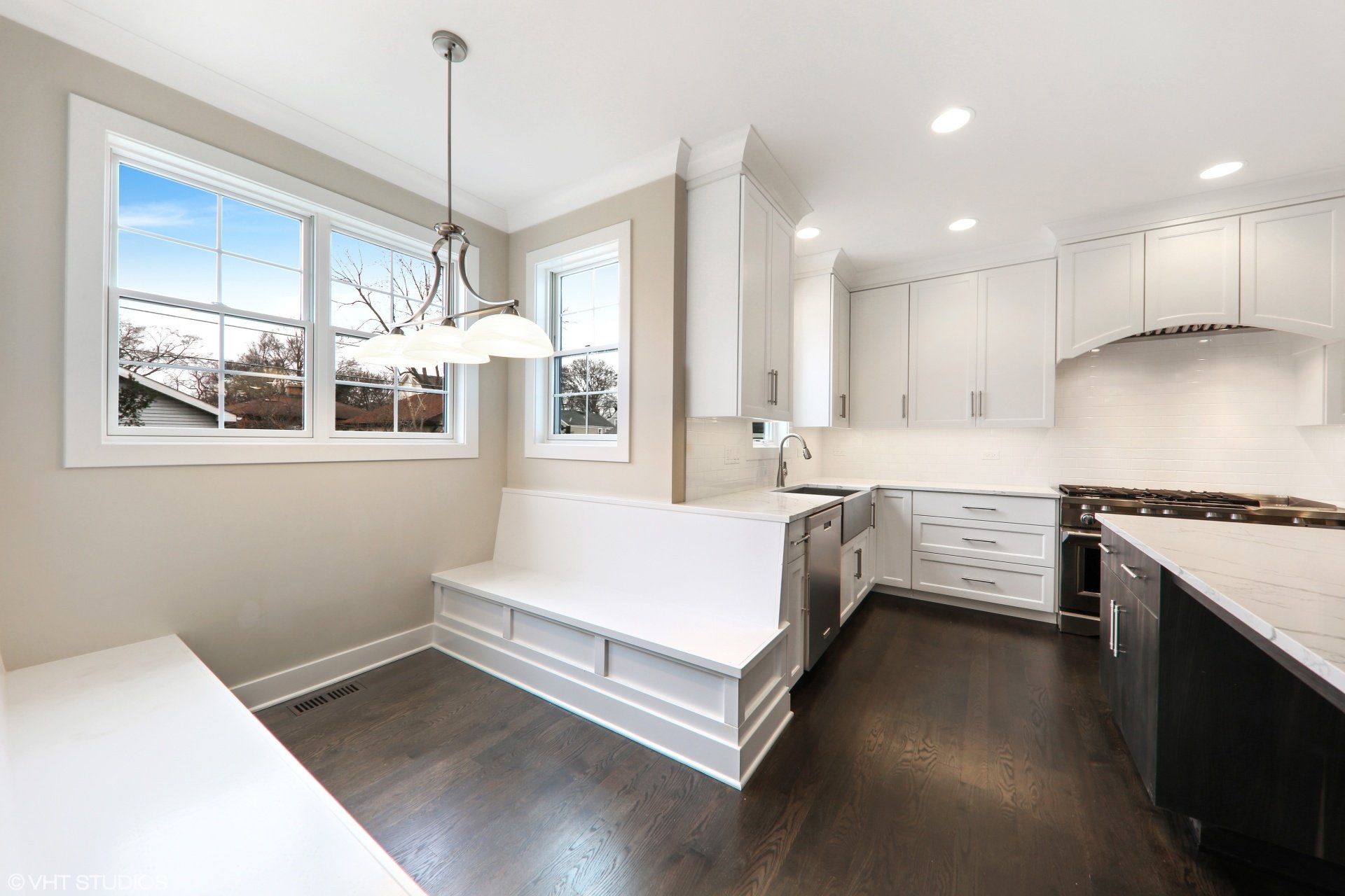 A kitchen with white cabinets and stainless steel appliances and a bench in the corner.