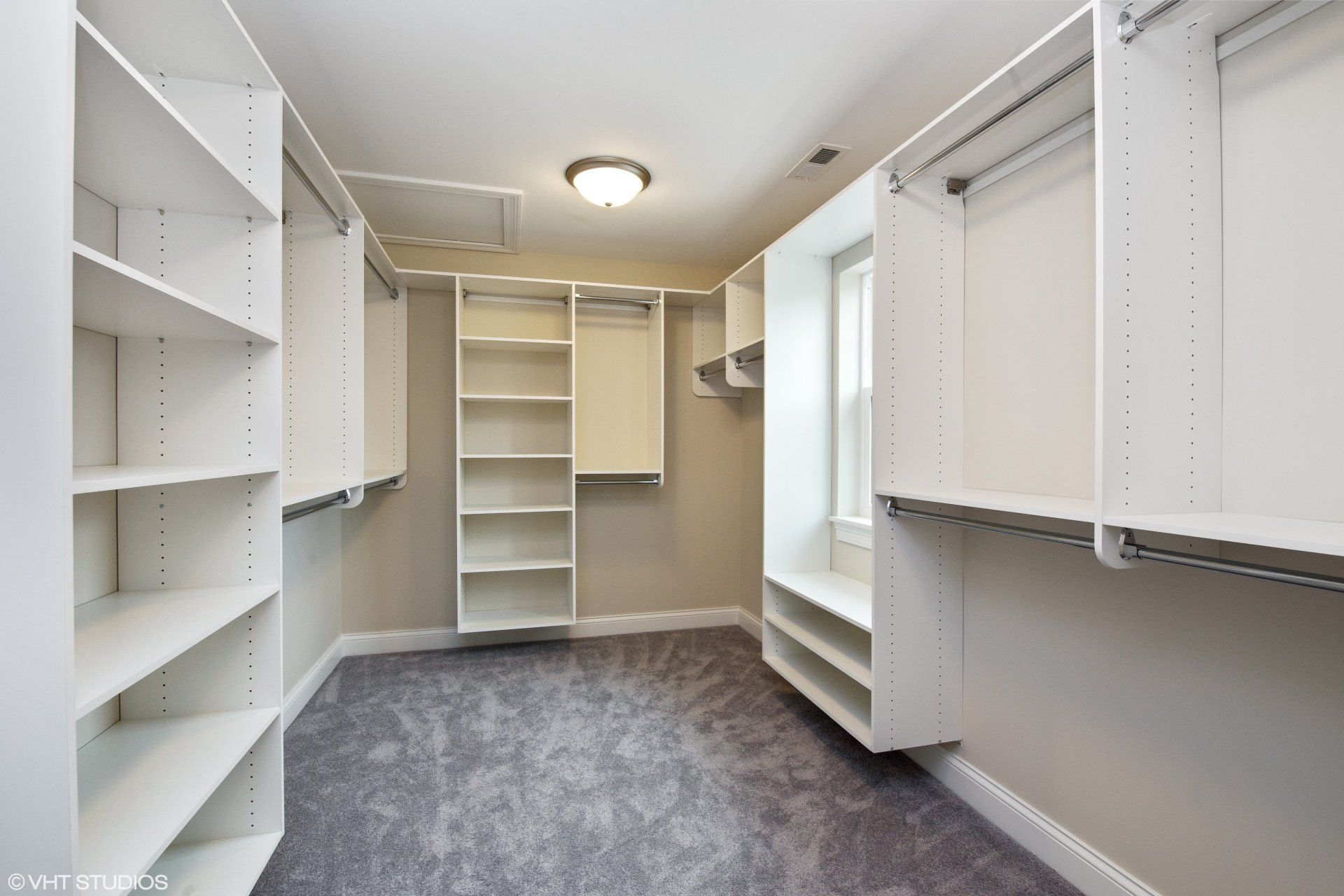 An empty walk in closet with white shelves and a window.
