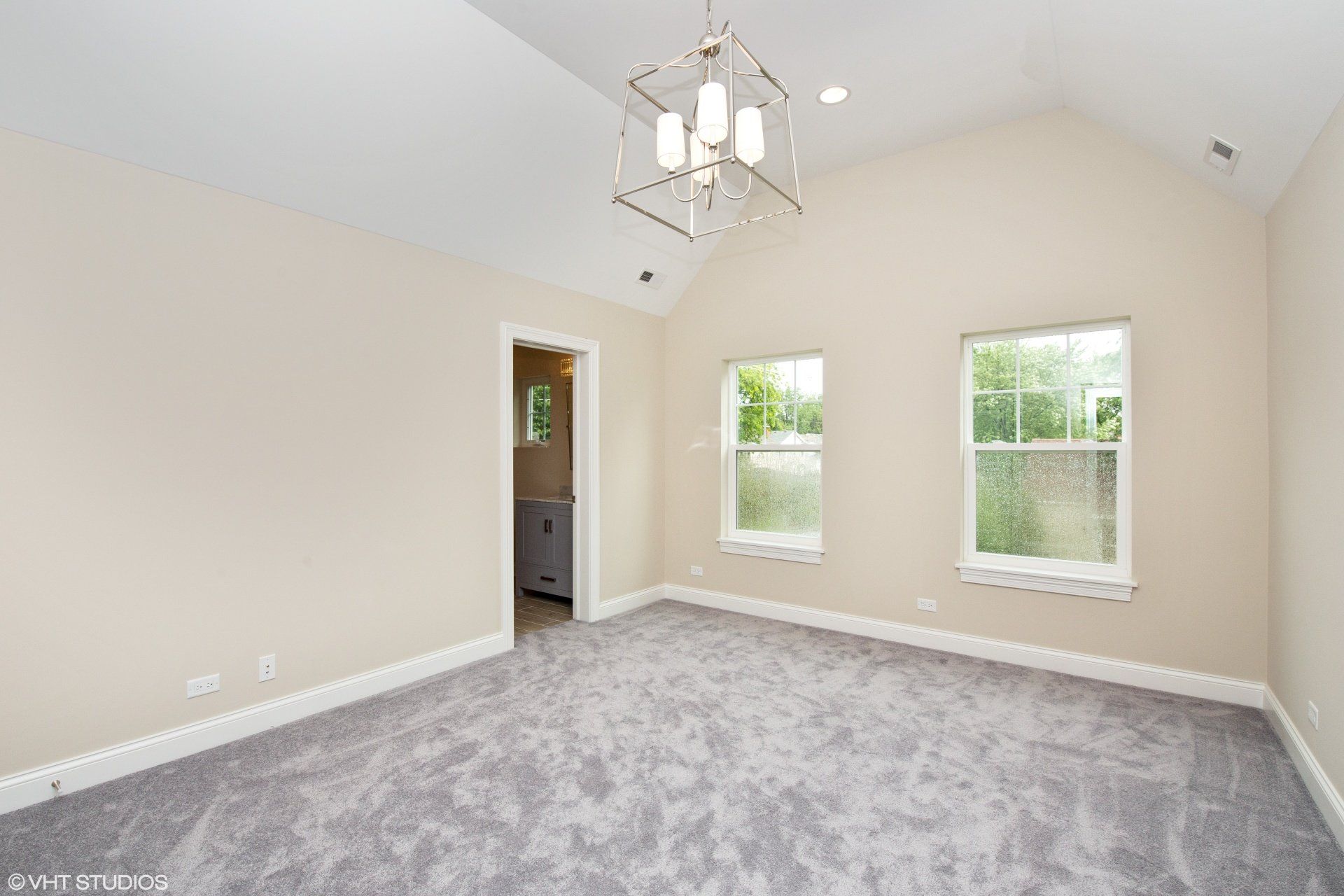 An empty bedroom with a chandelier and three windows.