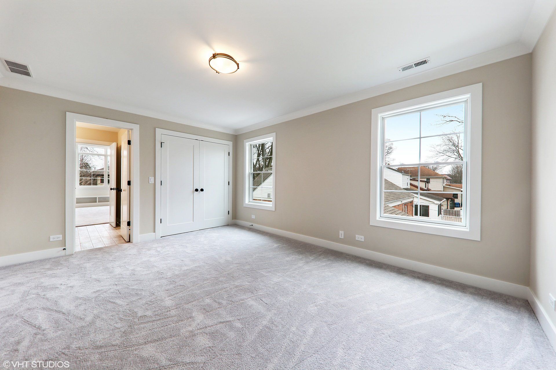 An empty bedroom with a carpeted floor and two windows.
