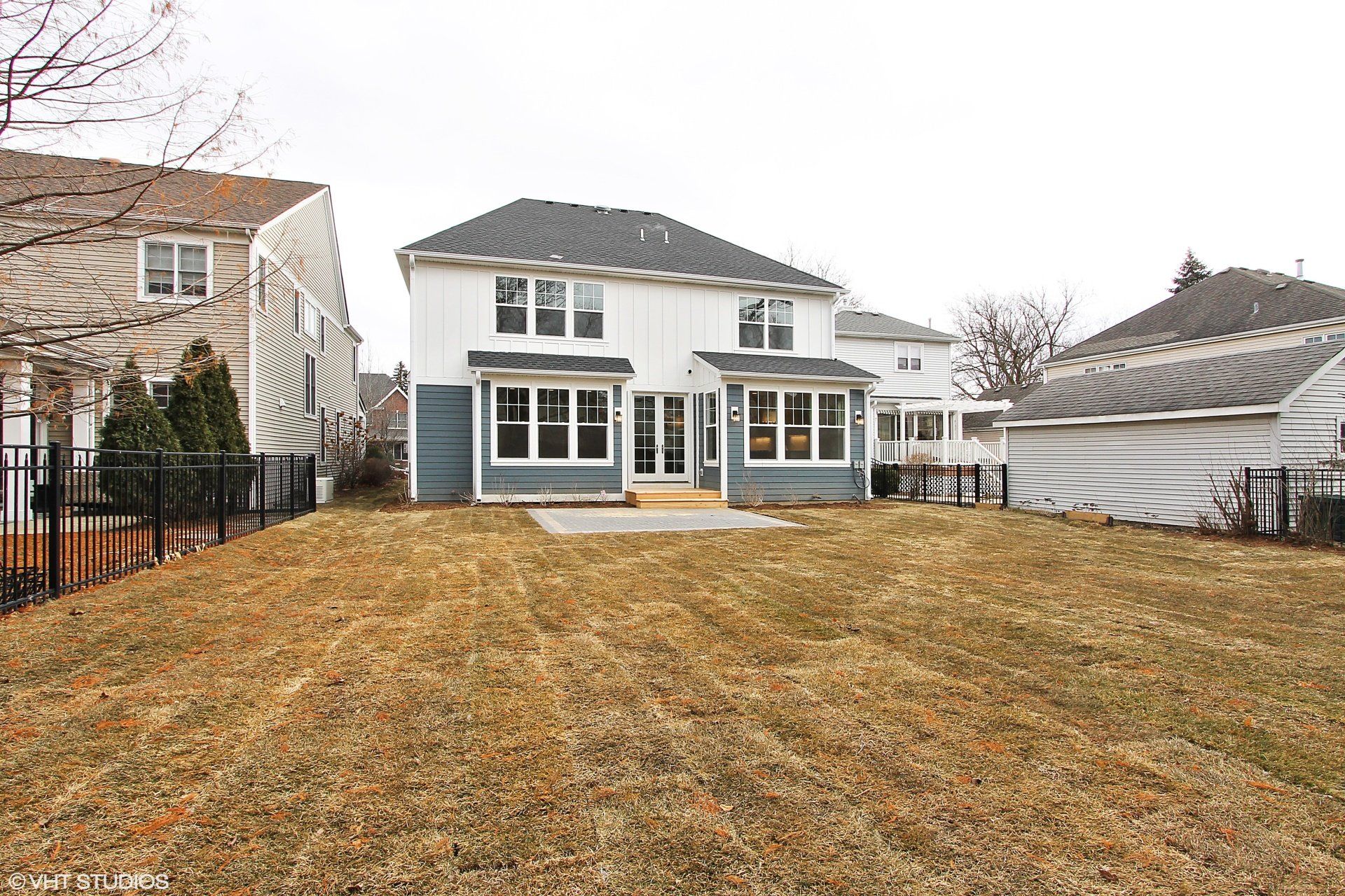 The backyard of a house with a large lawn and a fence.