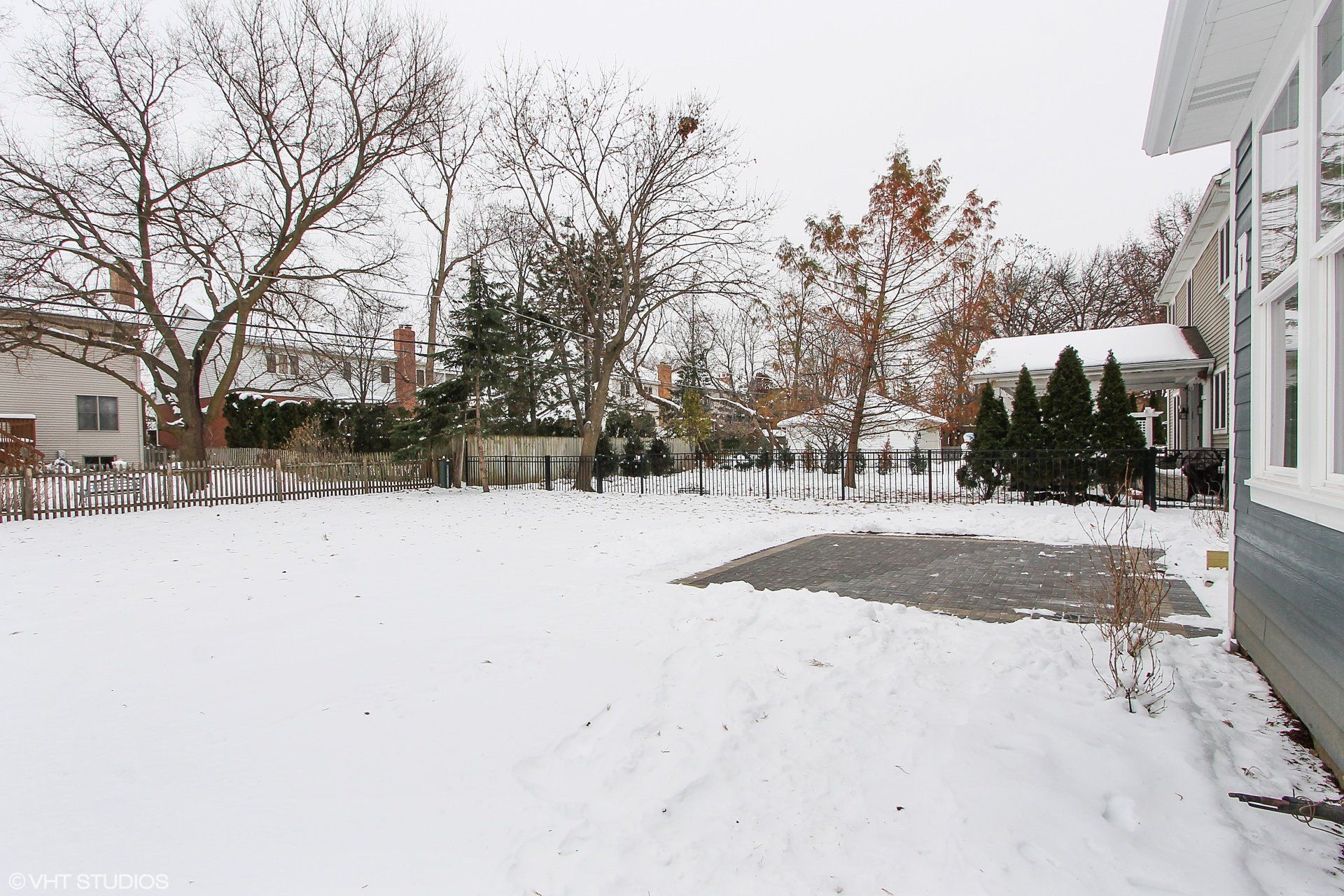 A snowy yard with a house and trees in the background.