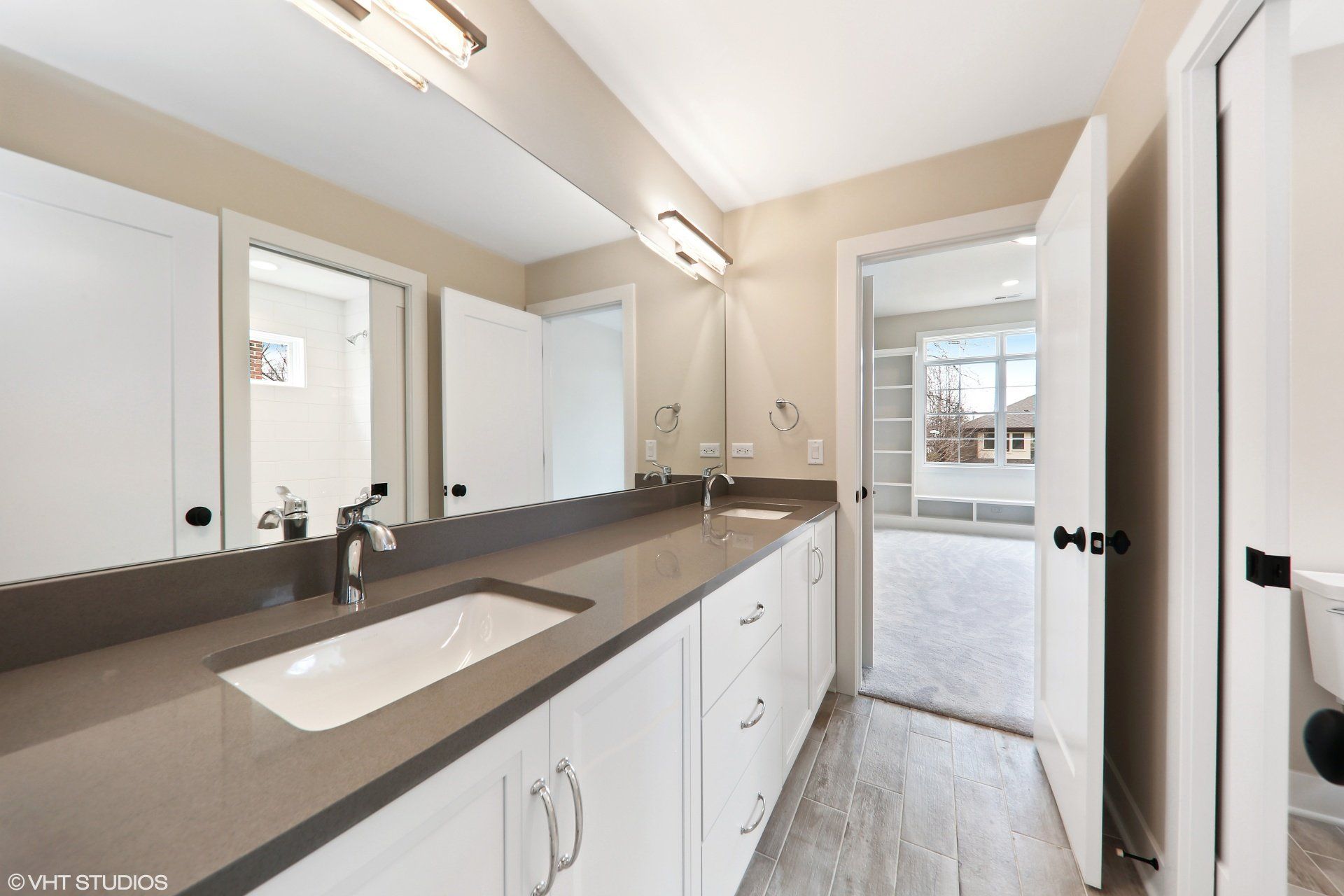 A bathroom with two sinks , two mirrors and a toilet.