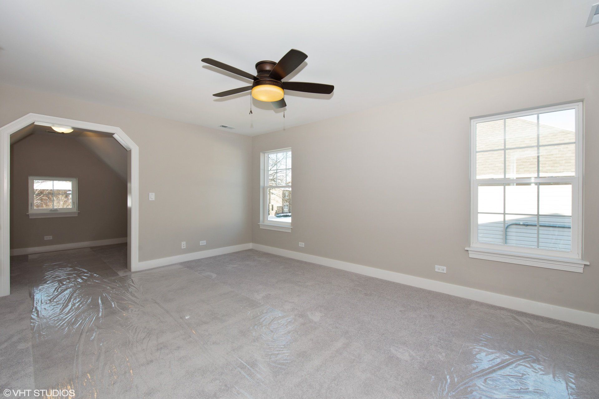 An empty room with a ceiling fan and two windows