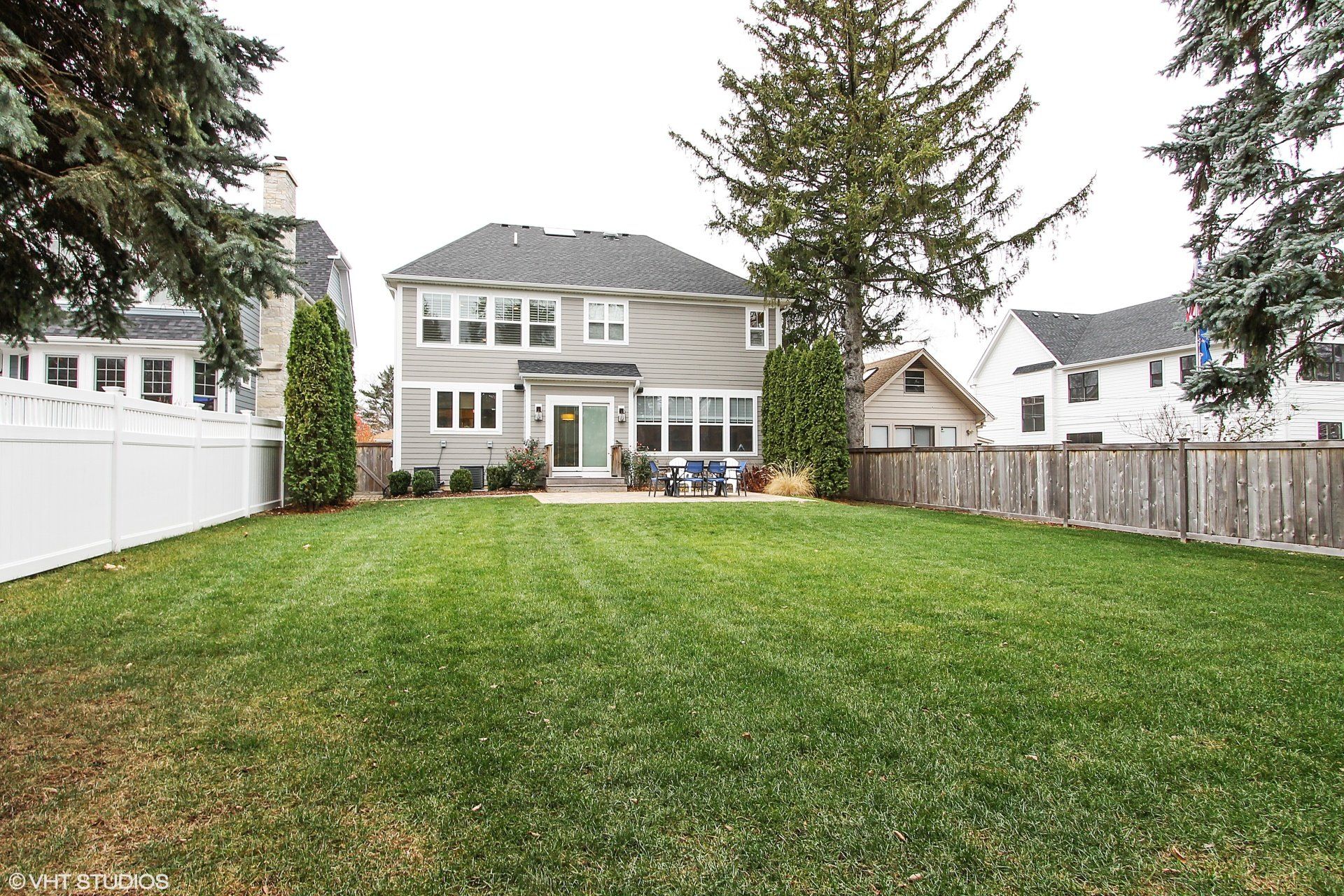 The backyard of a house with a large lawn and a white fence.