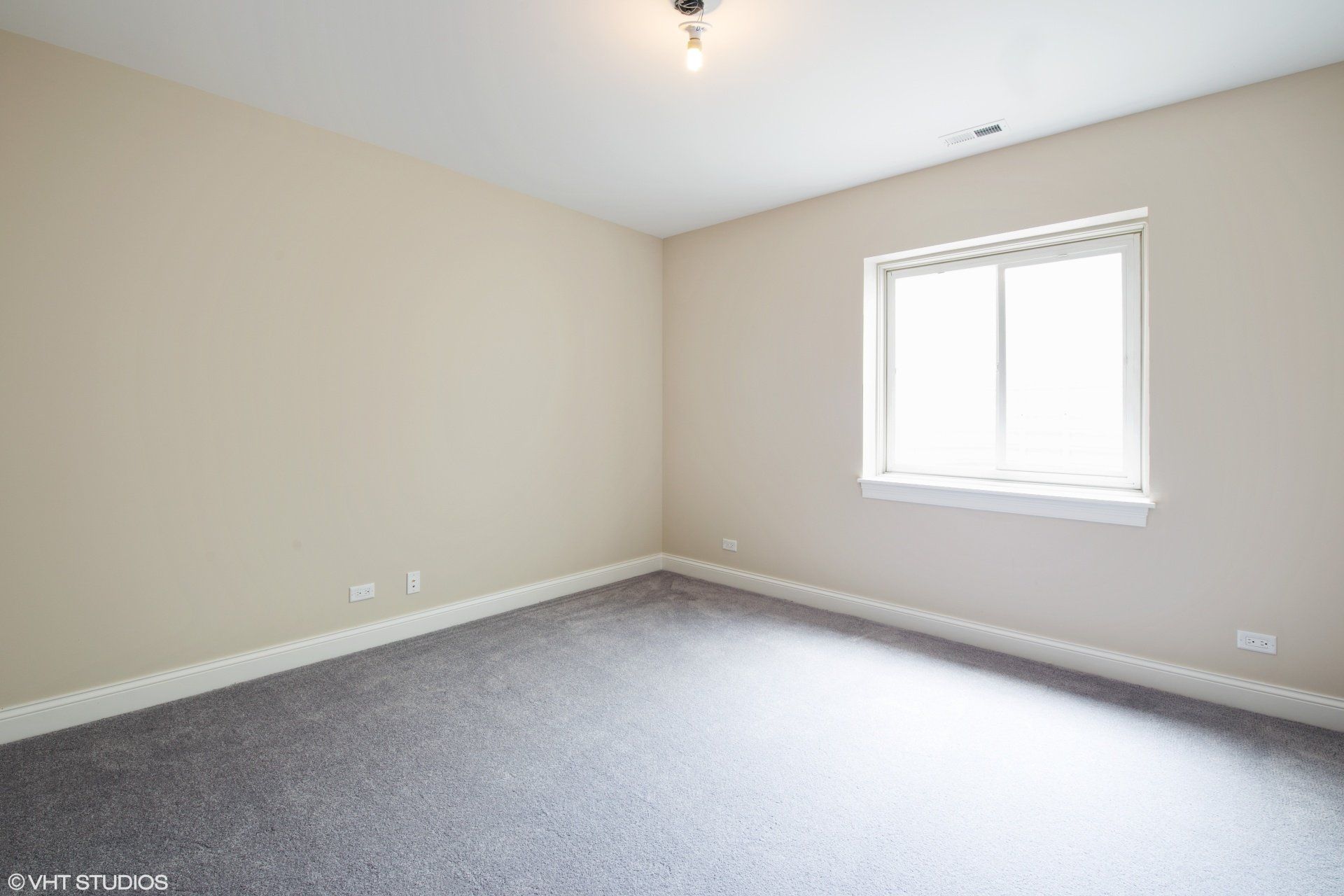 An empty room with a window and a gray carpet.