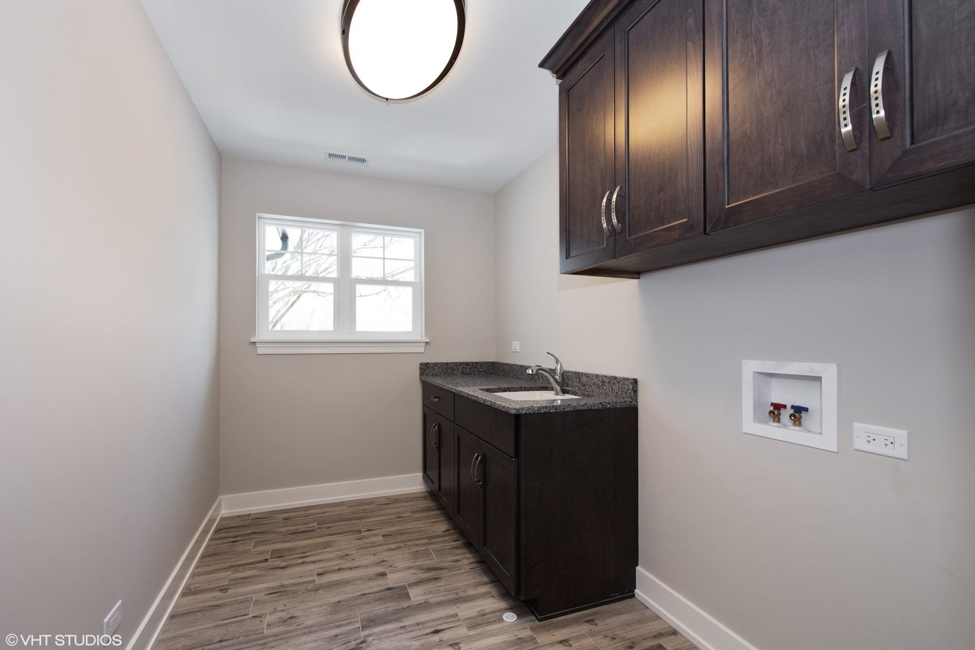 A laundry room with a sink , cabinets , and a window.