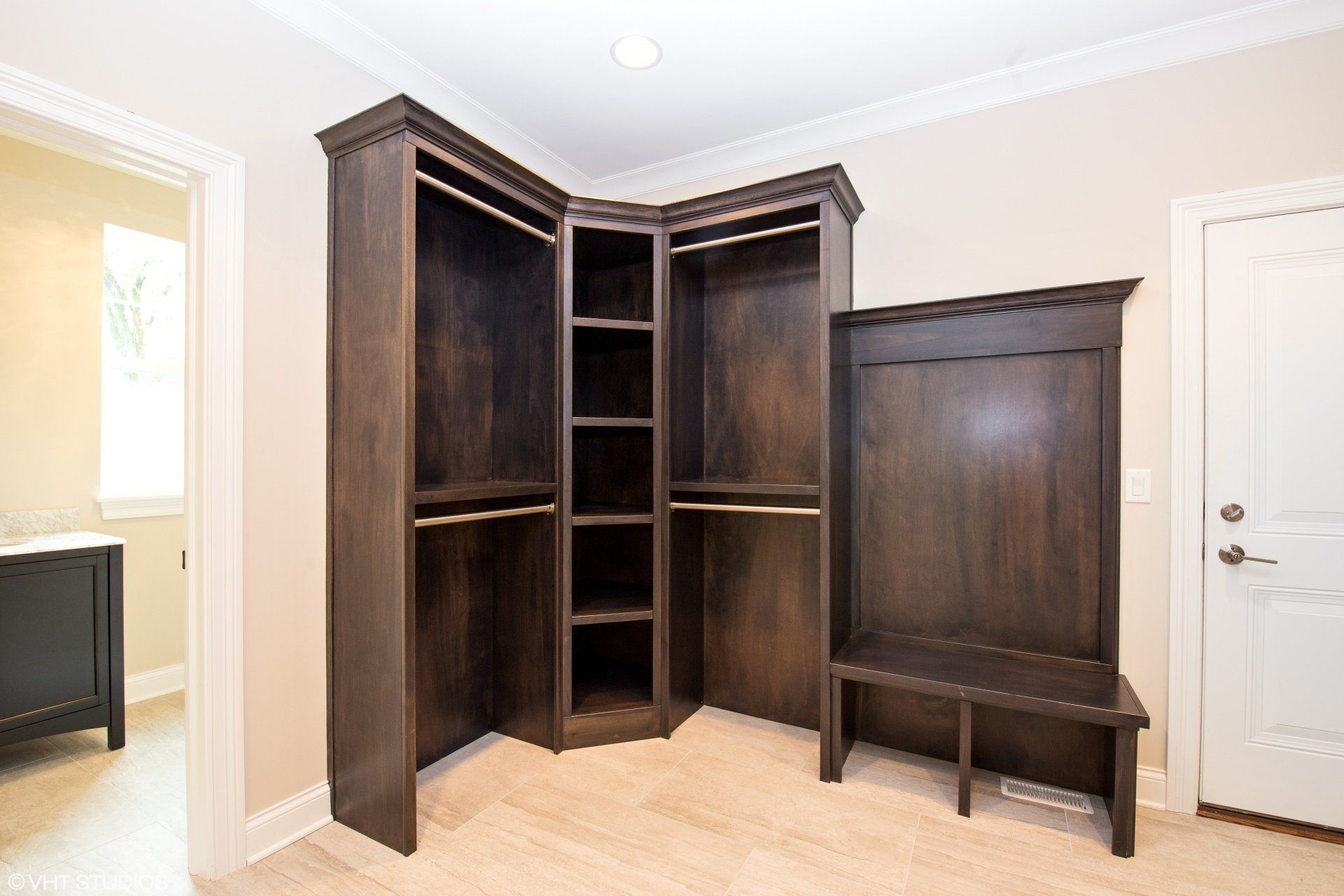 A walk in closet with wooden shelves and a bench.