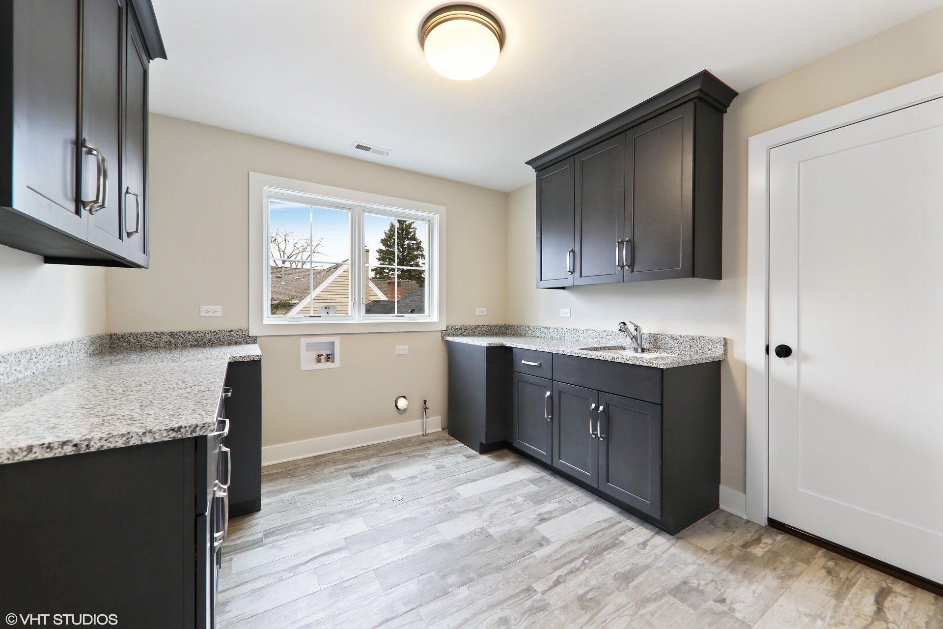 A laundry room with black cabinets , granite counter tops , and a window.