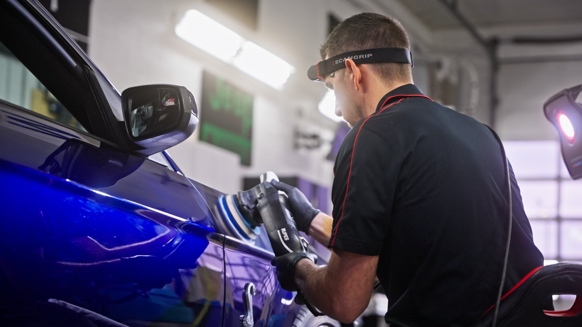 a man is polishing a blue car in a garage .