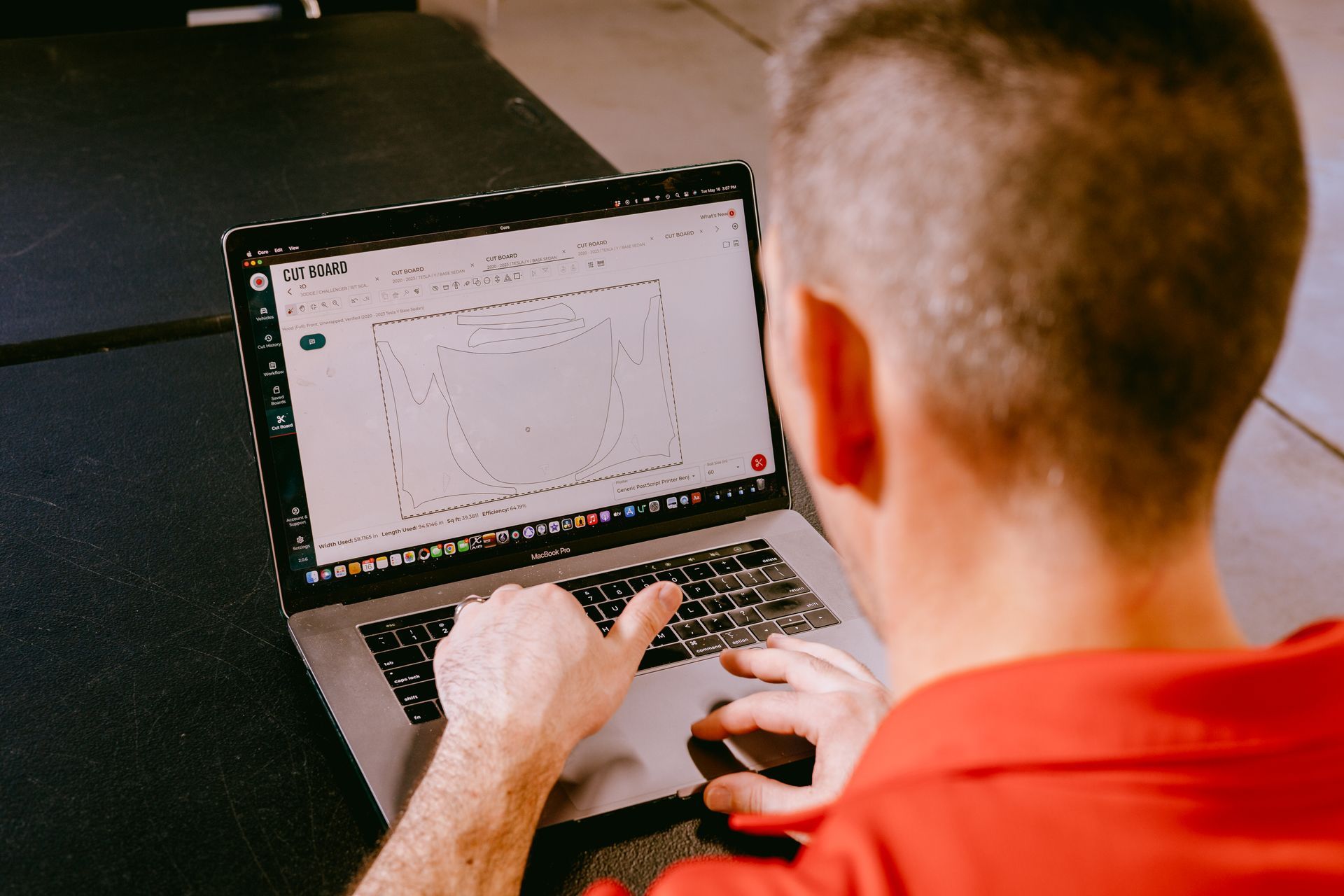 A man in a red shirt is typing on a laptop computer.
