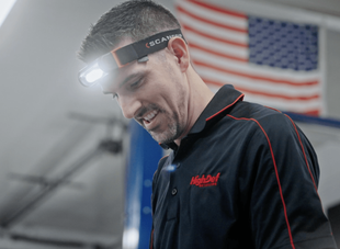 a man wearing a headlamp is smiling in front of an american flag .