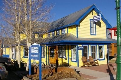 Yellow building with blue trim, signage for Caldwell Banker Realty, and a bike leaning nearby.
