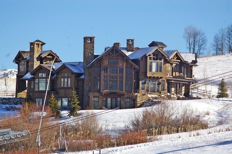 Large, rustic wooden house on a snow-covered hill, under a bright blue sky.