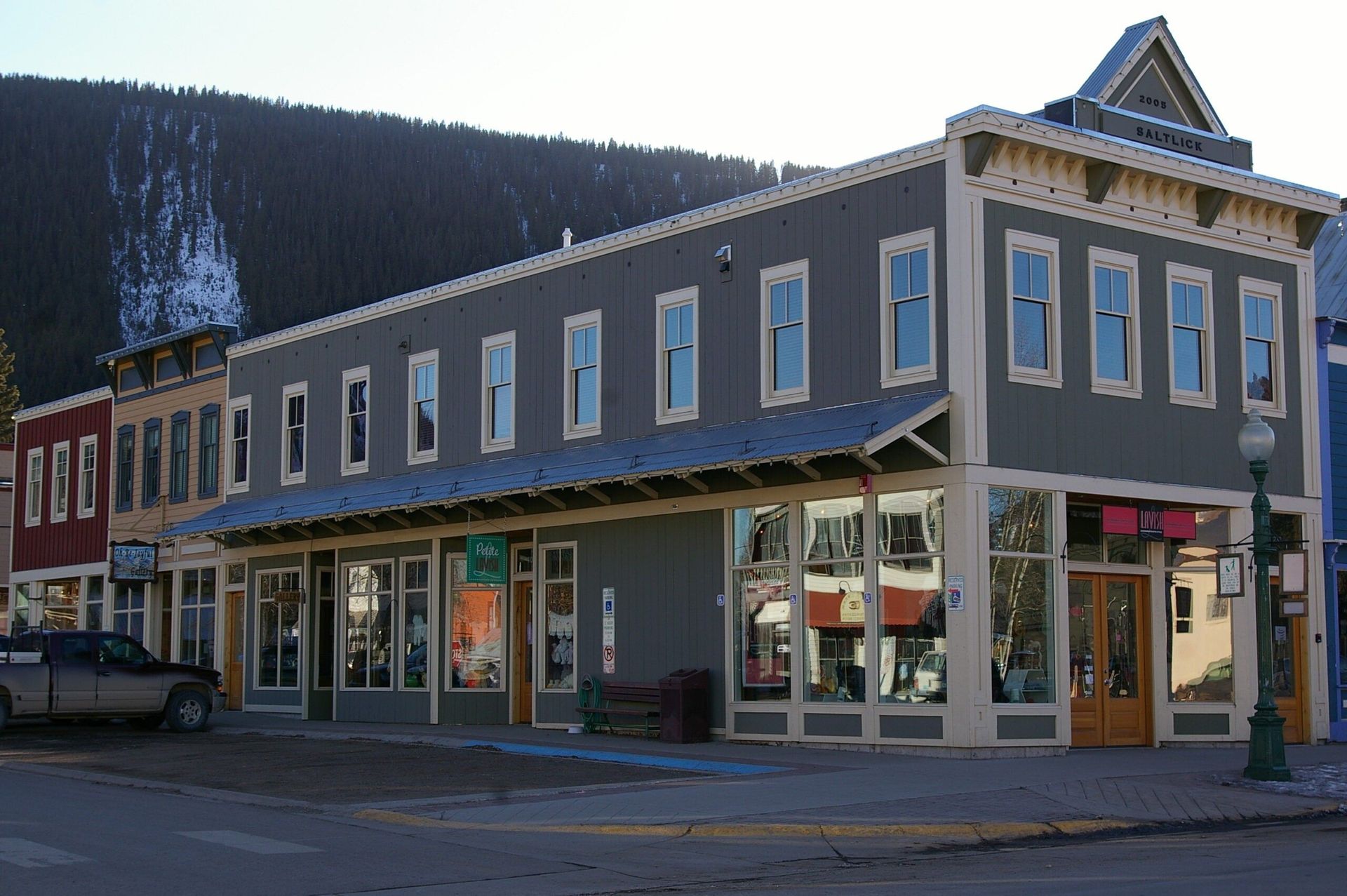 Gray two-story building with storefronts and light-colored trim, in a town with mountains in the background.