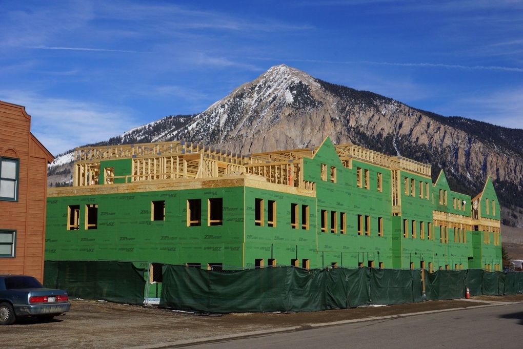 Construction of a multi-story building with green siding and a mountain backdrop.