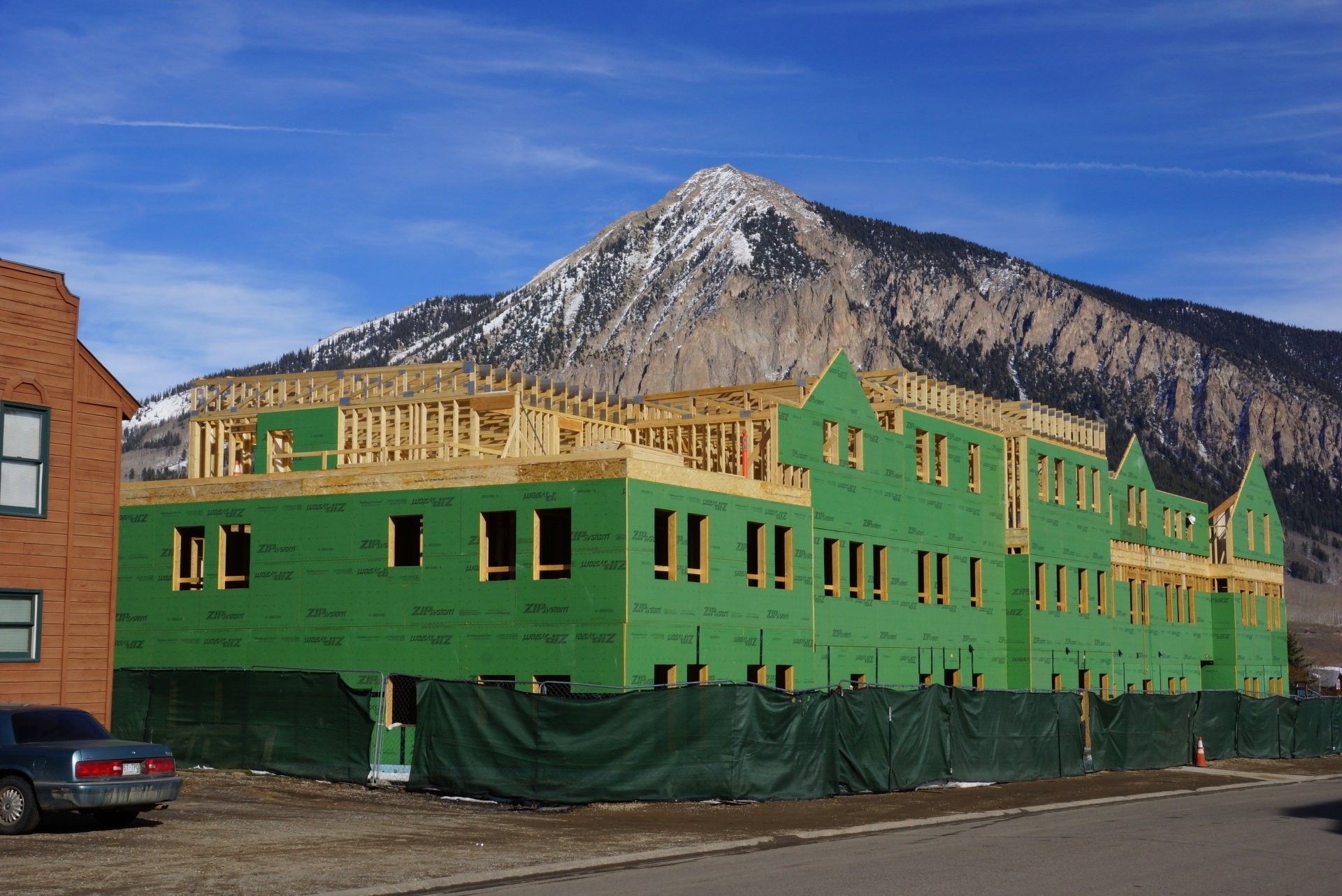 Construction of a multi-story building with green siding and a mountain backdrop.