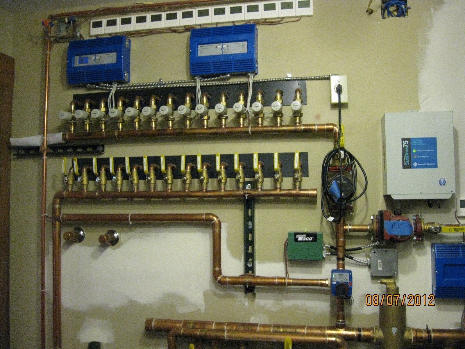 Copper plumbing manifold system on a wall, blue electrical boxes, and multiple valves.