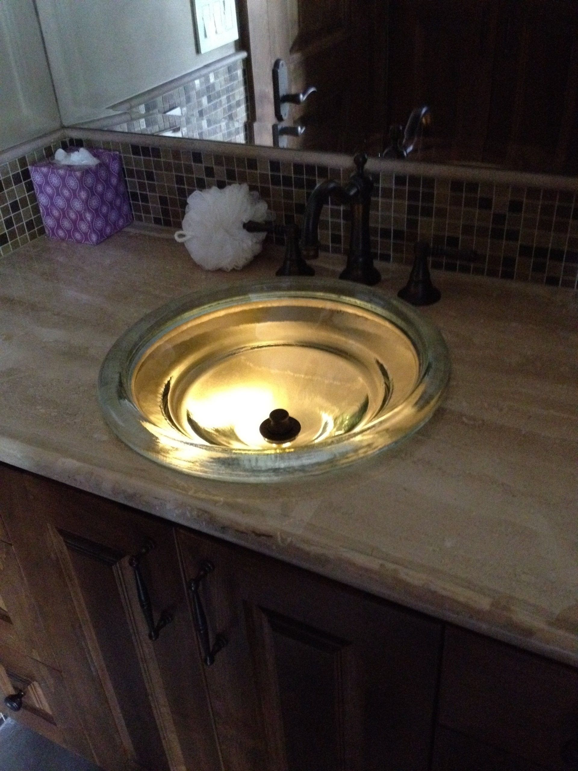 Glass vessel sink on a brown countertop with dark fixtures, set in a bathroom.