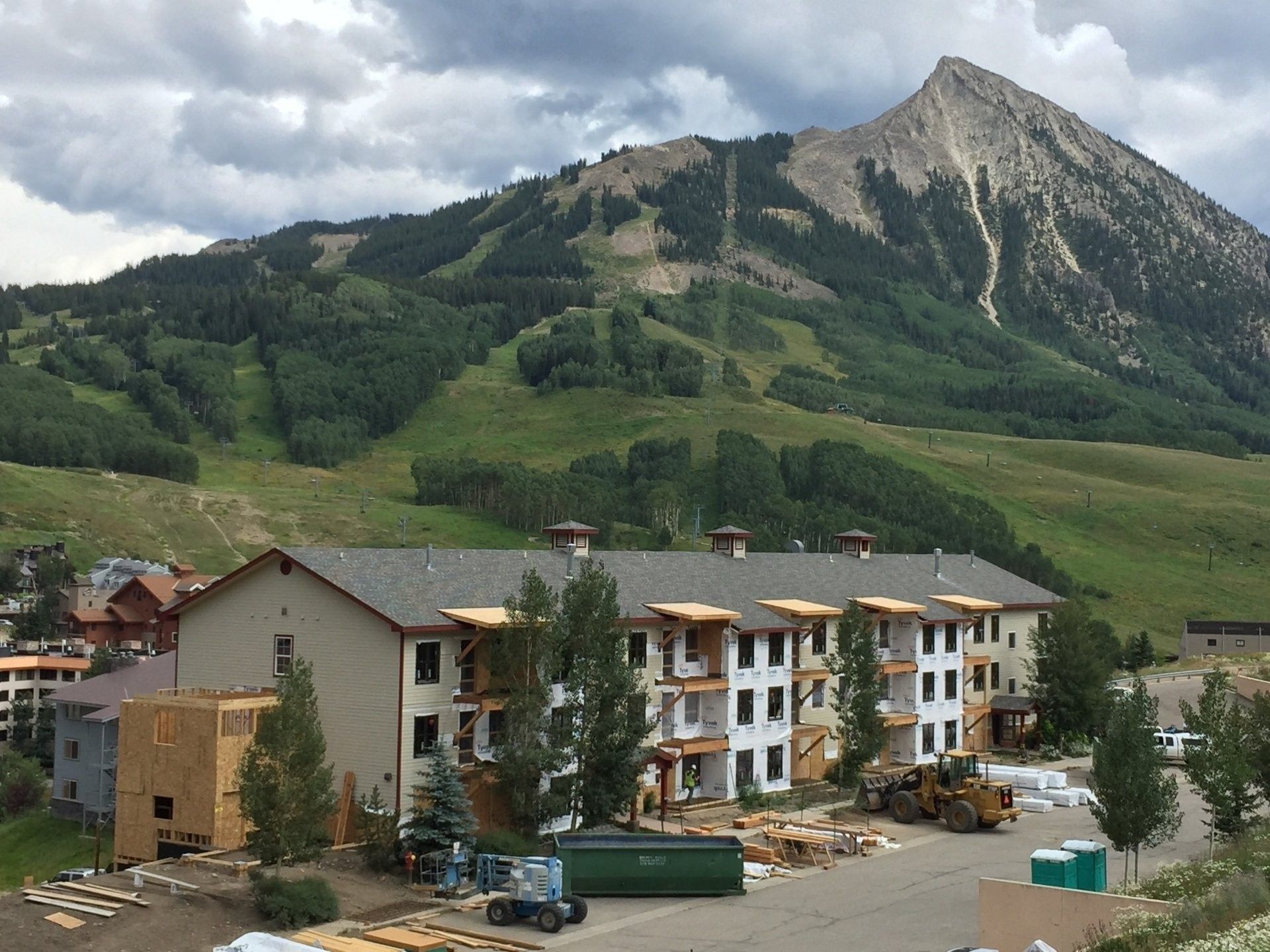 Building construction against a backdrop of a mountain with green slopes and a cloudy sky.
