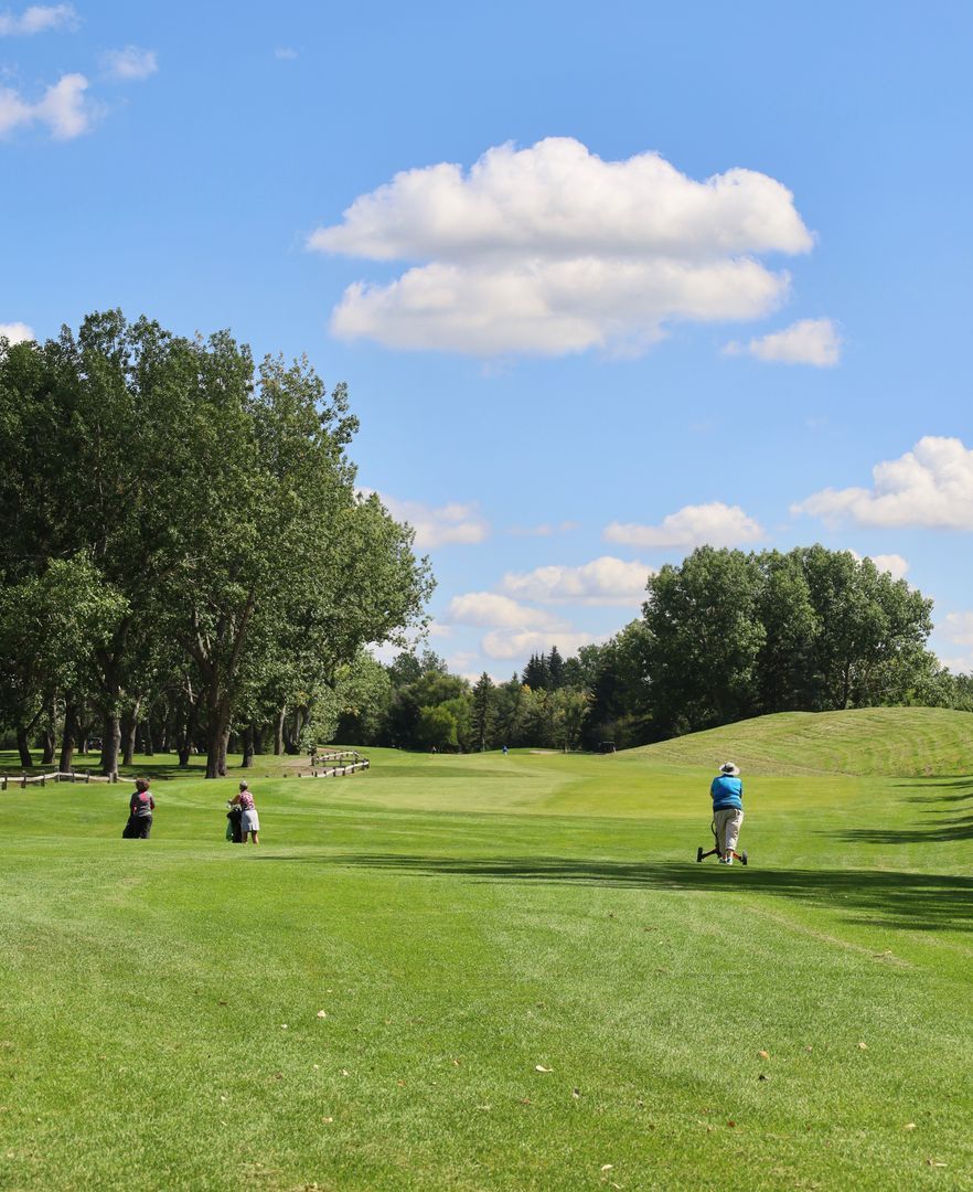 Golfers on a green course under a bright blue sky with fluffy clouds.