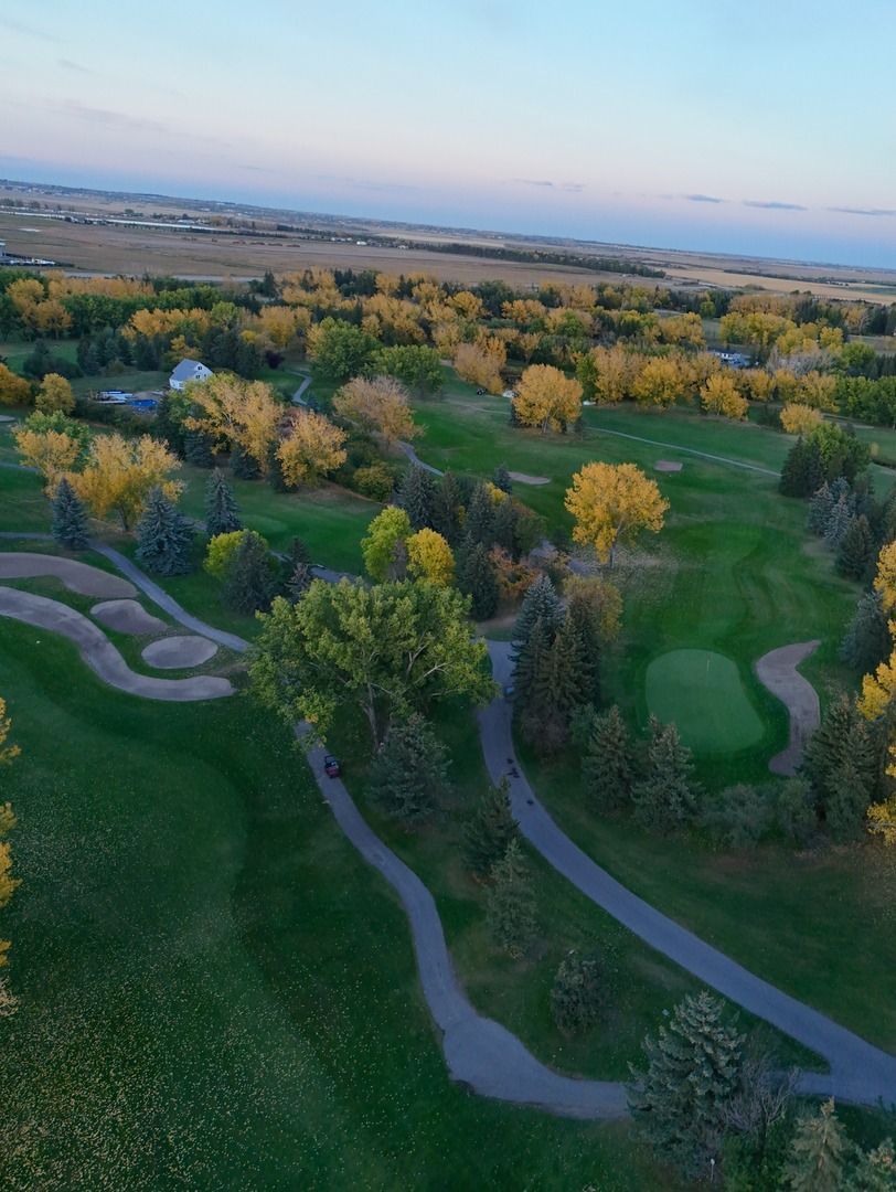 Aerial view of a green golf course with winding paths and scattered trees turning yellow in autumn.