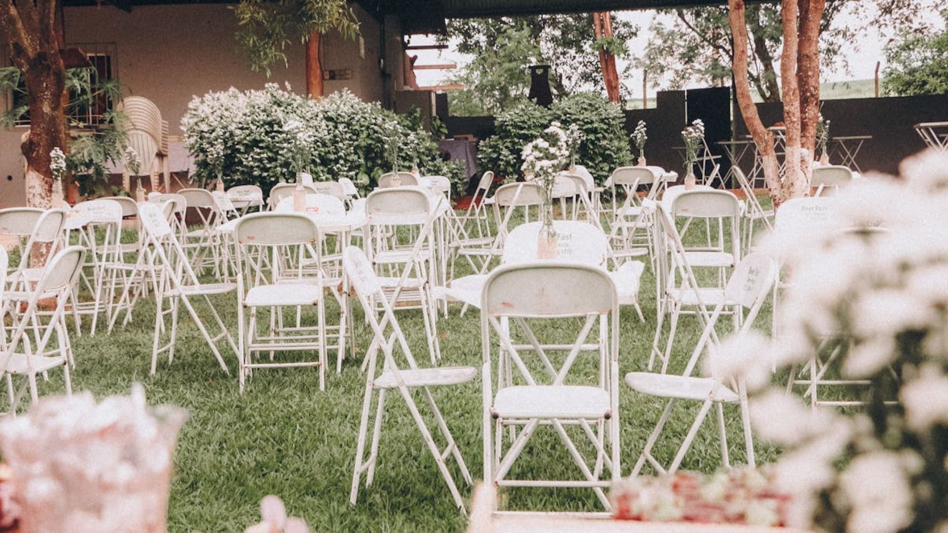 Sillas plegables blancas dispuestas en un jardín para un evento al aire libre, con flores en primer plano.