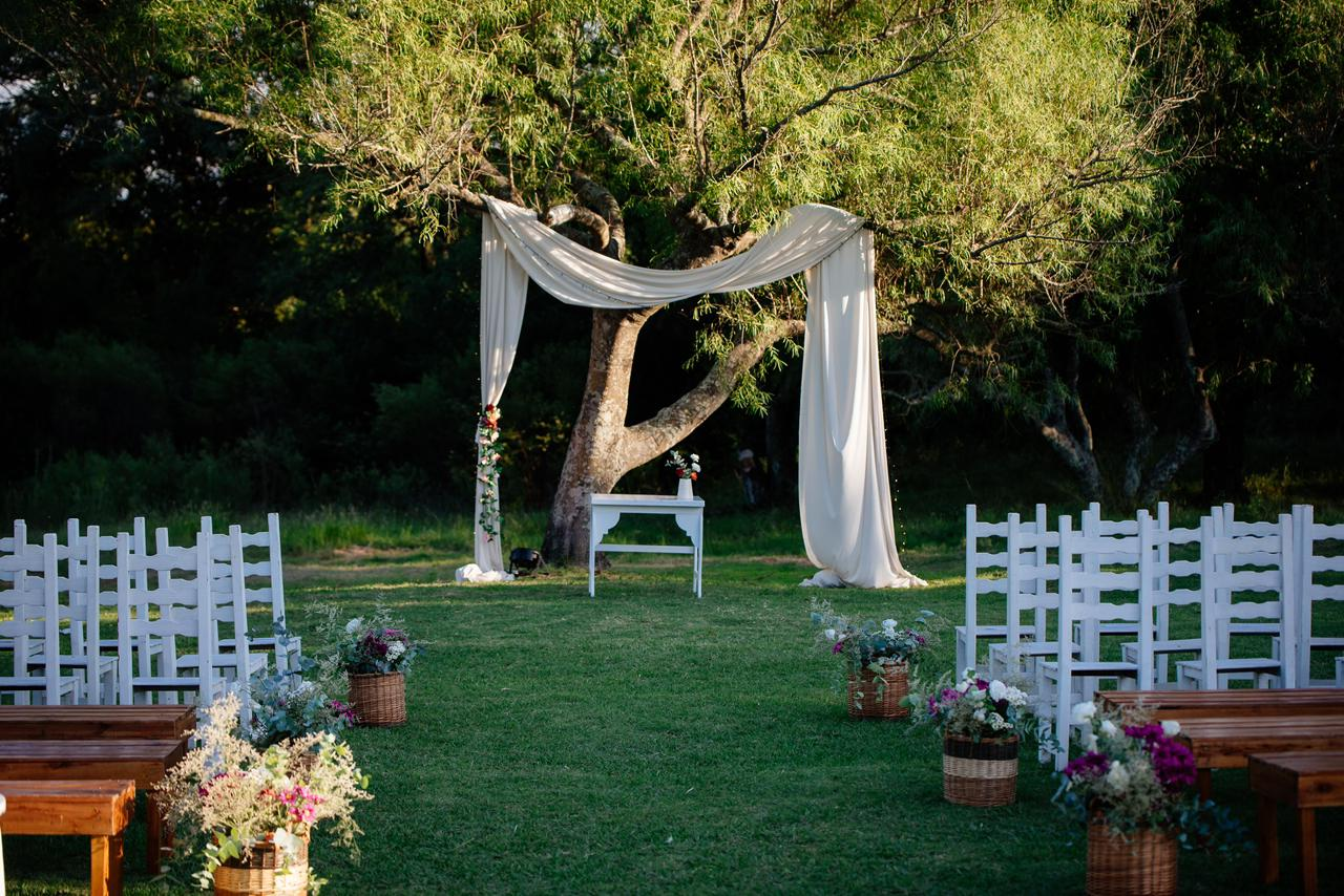 Montaje para una ceremonia de boda al aire libre con sillas blancas, arreglos florales 