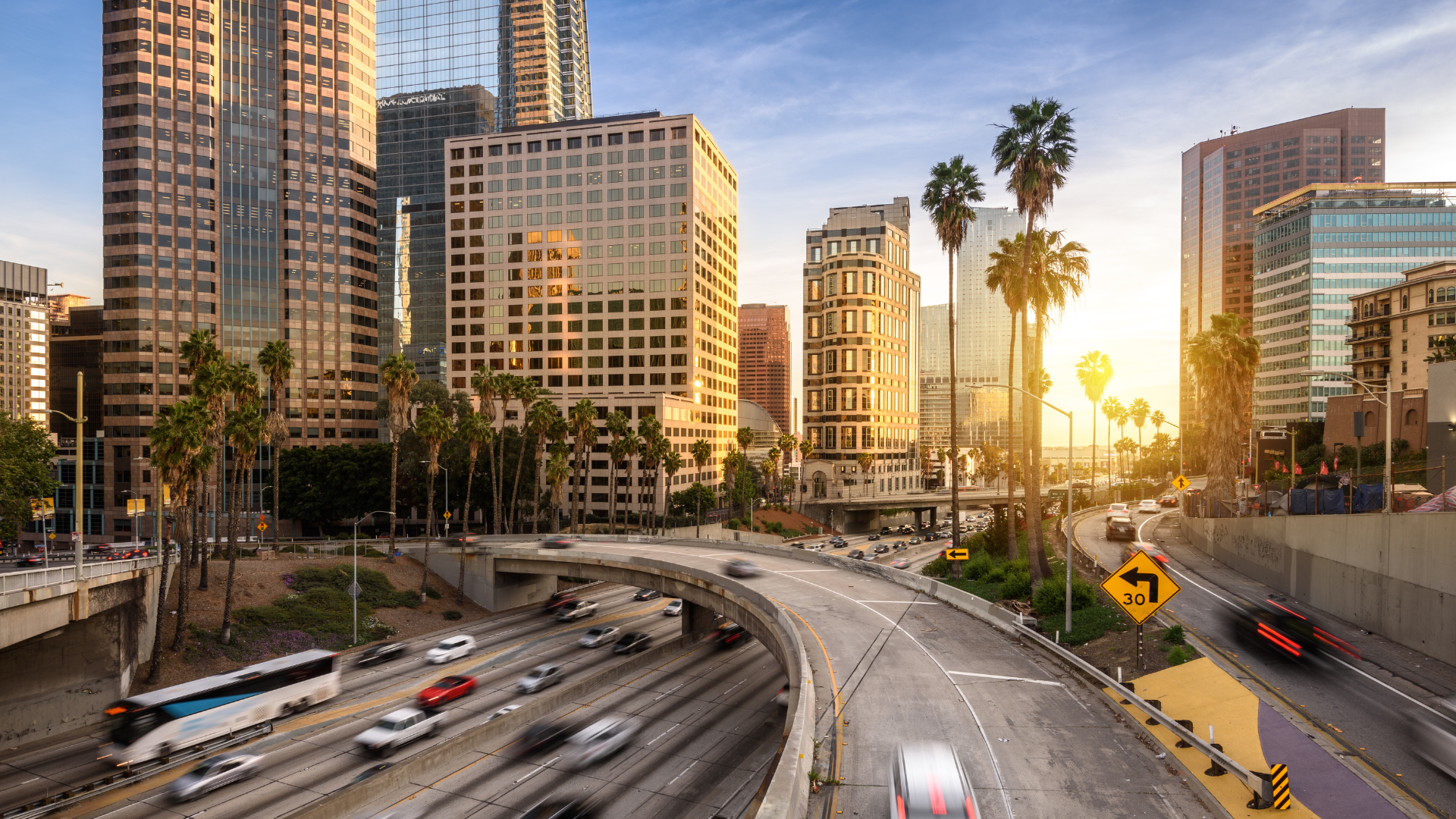 A truck is driving down a highway in a city at sunset.