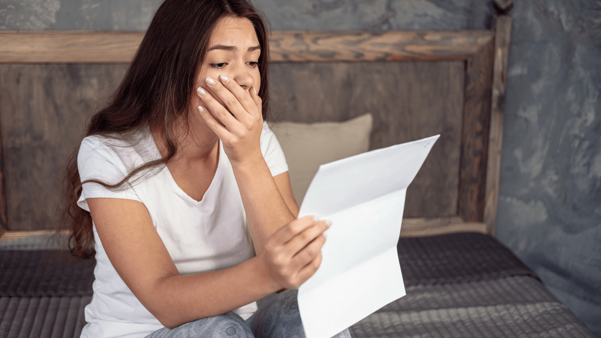 A woman is sitting on a bed reading a letter.