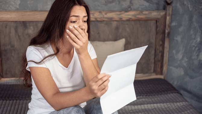 A woman is sitting on a bed reading a letter.