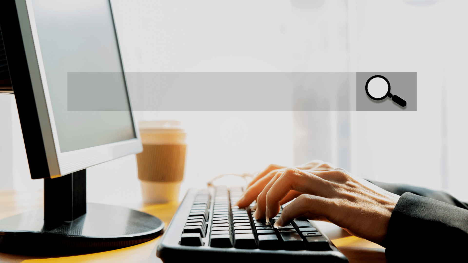 A person is typing on a keyboard in front of a computer monitor.