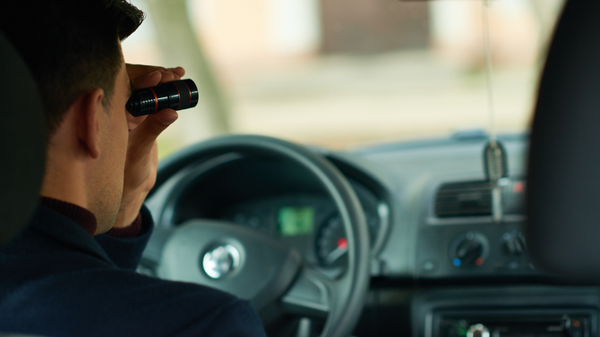 A man is looking through binoculars while driving a car.