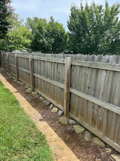 A wooden fence is surrounded by rocks and grass in a backyard.