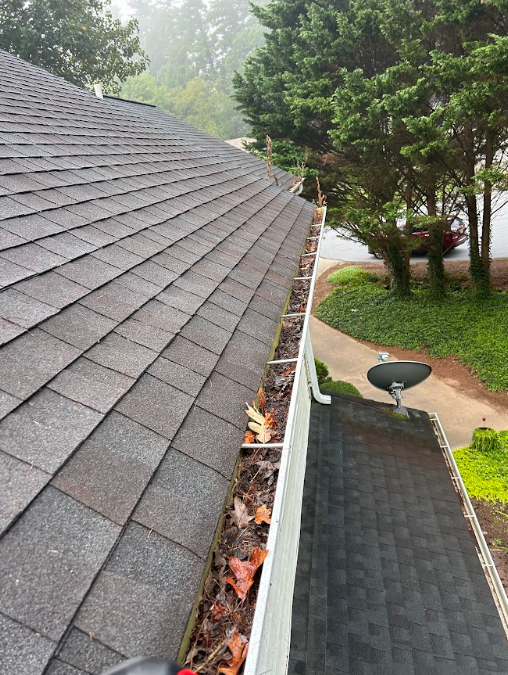 A gutter with leaves on it is on the roof of a house.