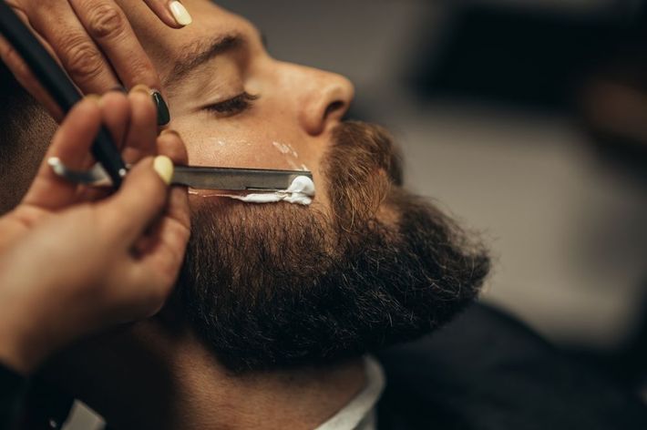 A man is getting his beard shaved by a barber with a razor.