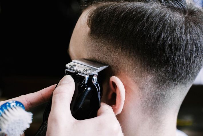 A man is getting his hair cut by a barber with a clipper.