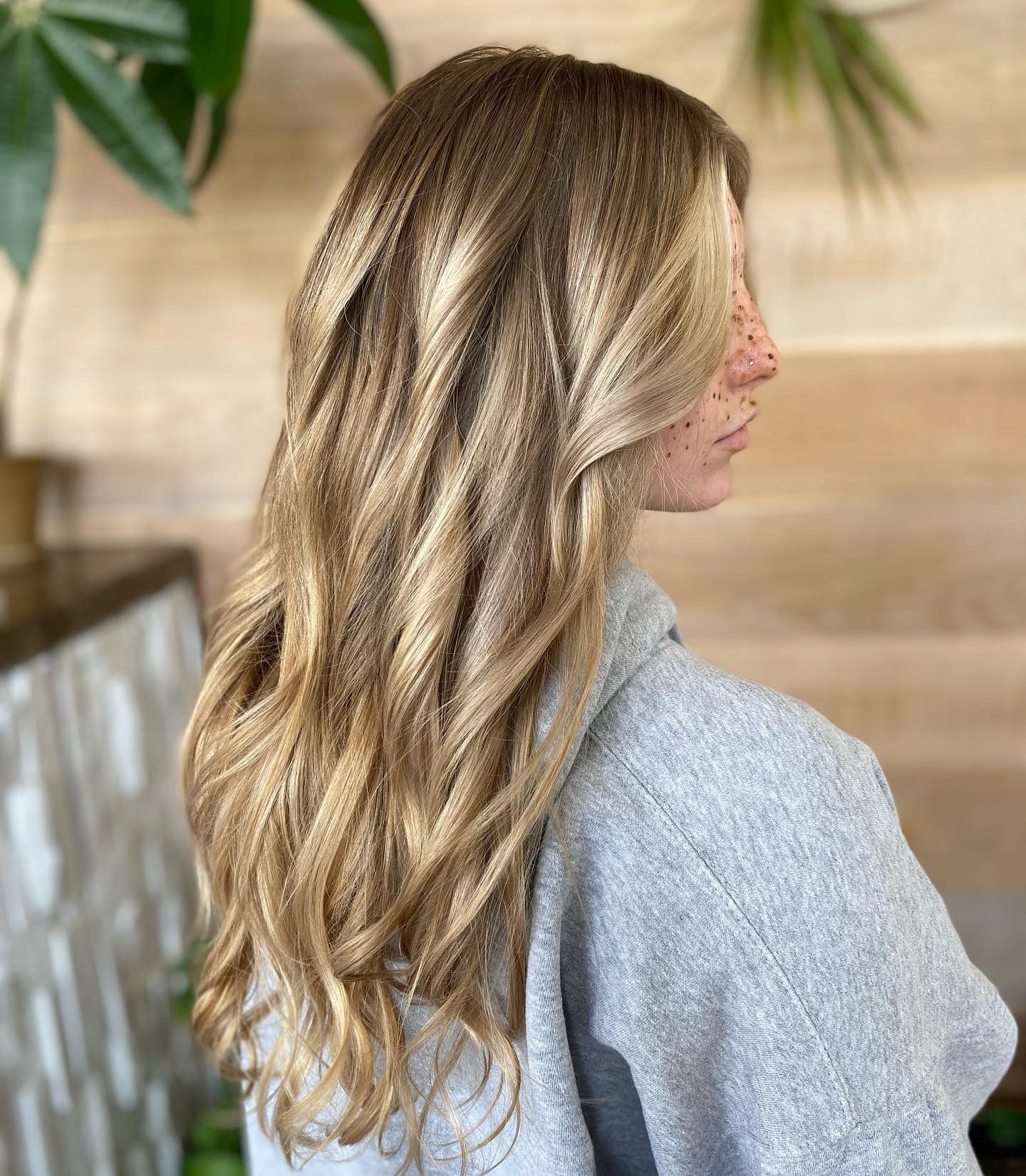 A woman with long blonde hair is standing in front of a wooden wall.