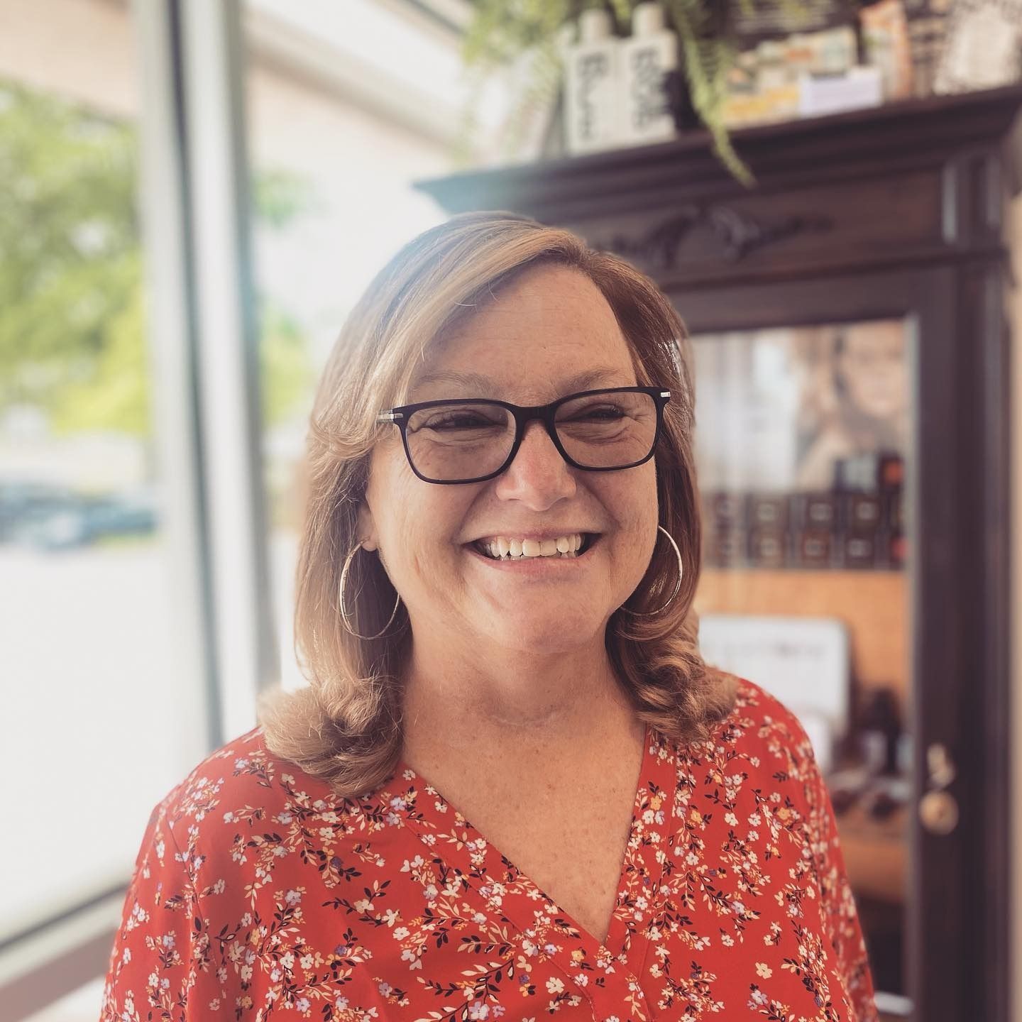 A woman wearing glasses and a red shirt is smiling for the camera.