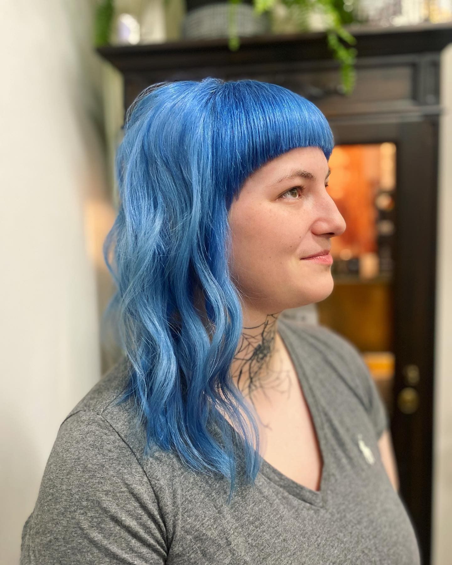 A woman with blue hair is wearing a gray shirt.
