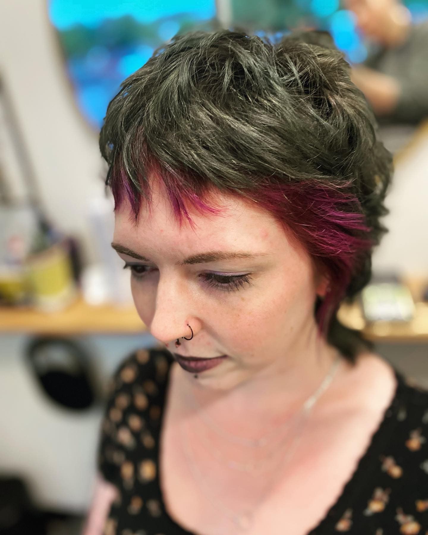 A woman with short hair and a nose ring is wearing a black shirt.