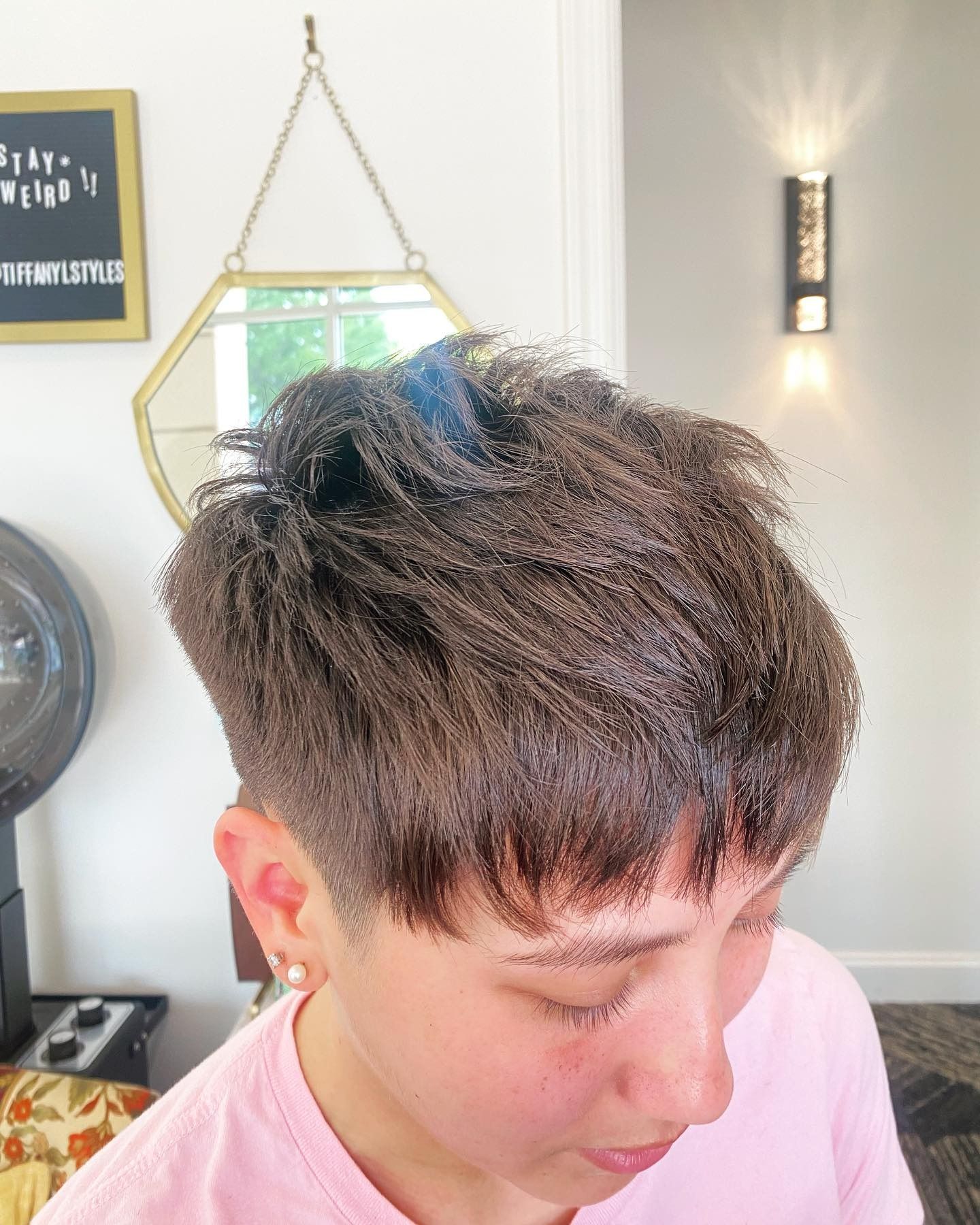 A woman in a pink shirt is getting her hair cut in a salon.