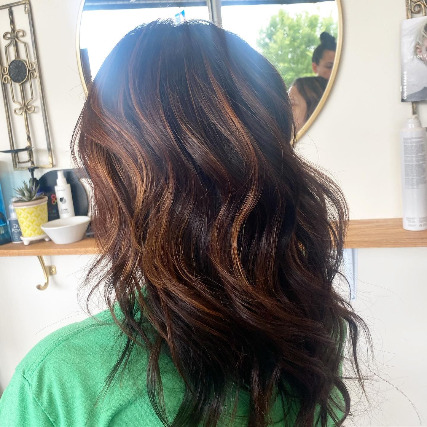 A woman in a green shirt is looking at her hair in front of a mirror
