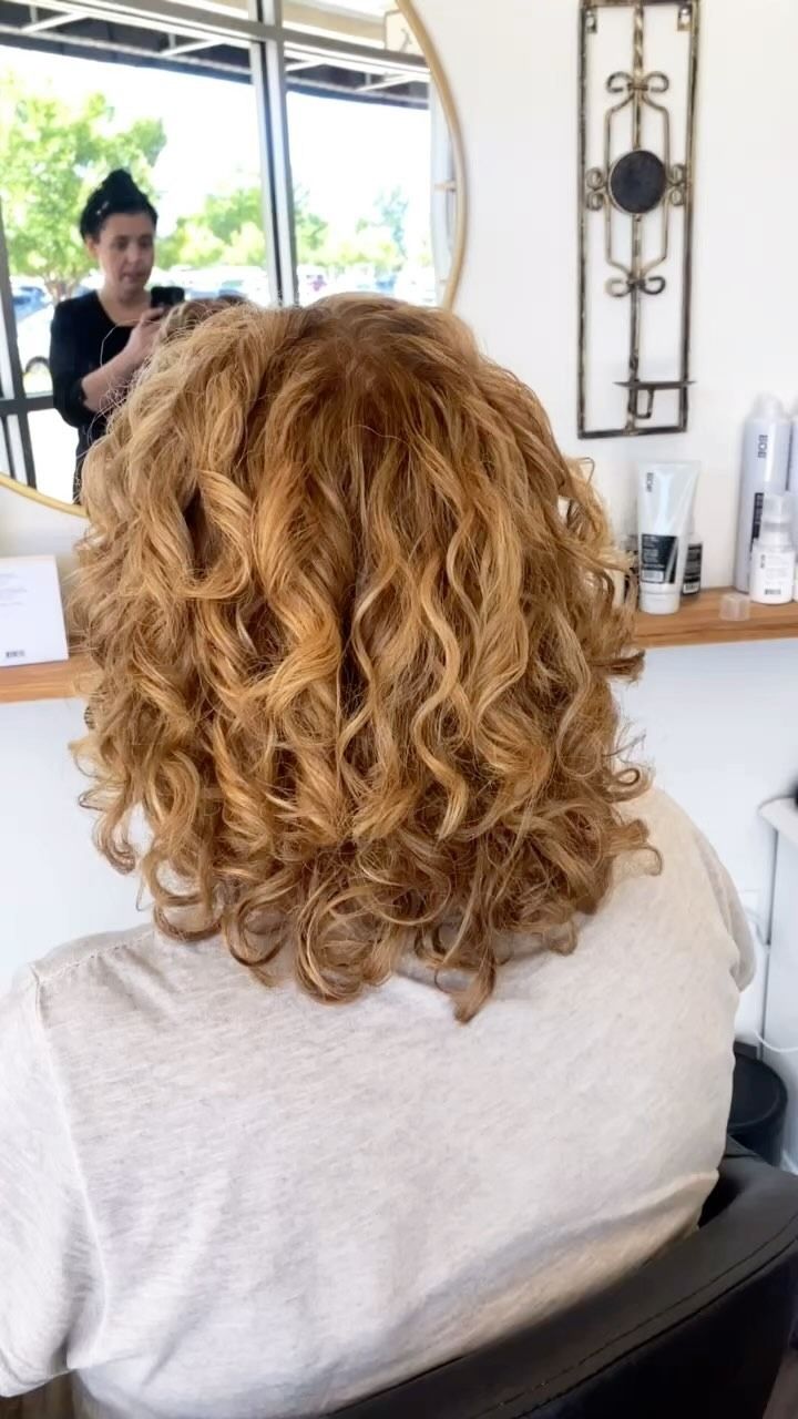 A woman with curly hair is sitting in a chair in front of a mirror.