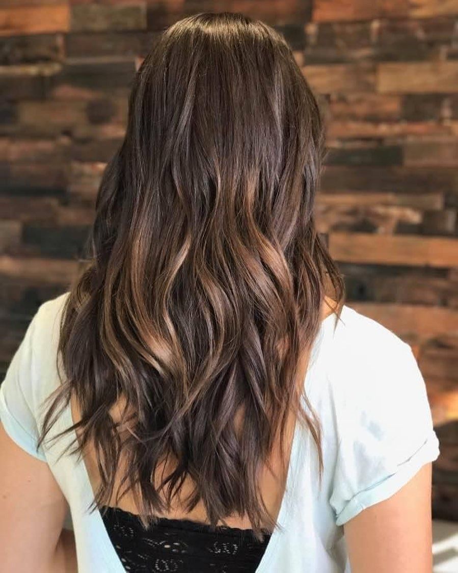 A woman with long brown hair is sitting in front of a wooden wall.