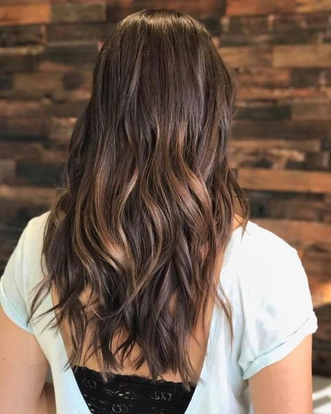 A woman with long brown hair is sitting in front of a wooden wall.