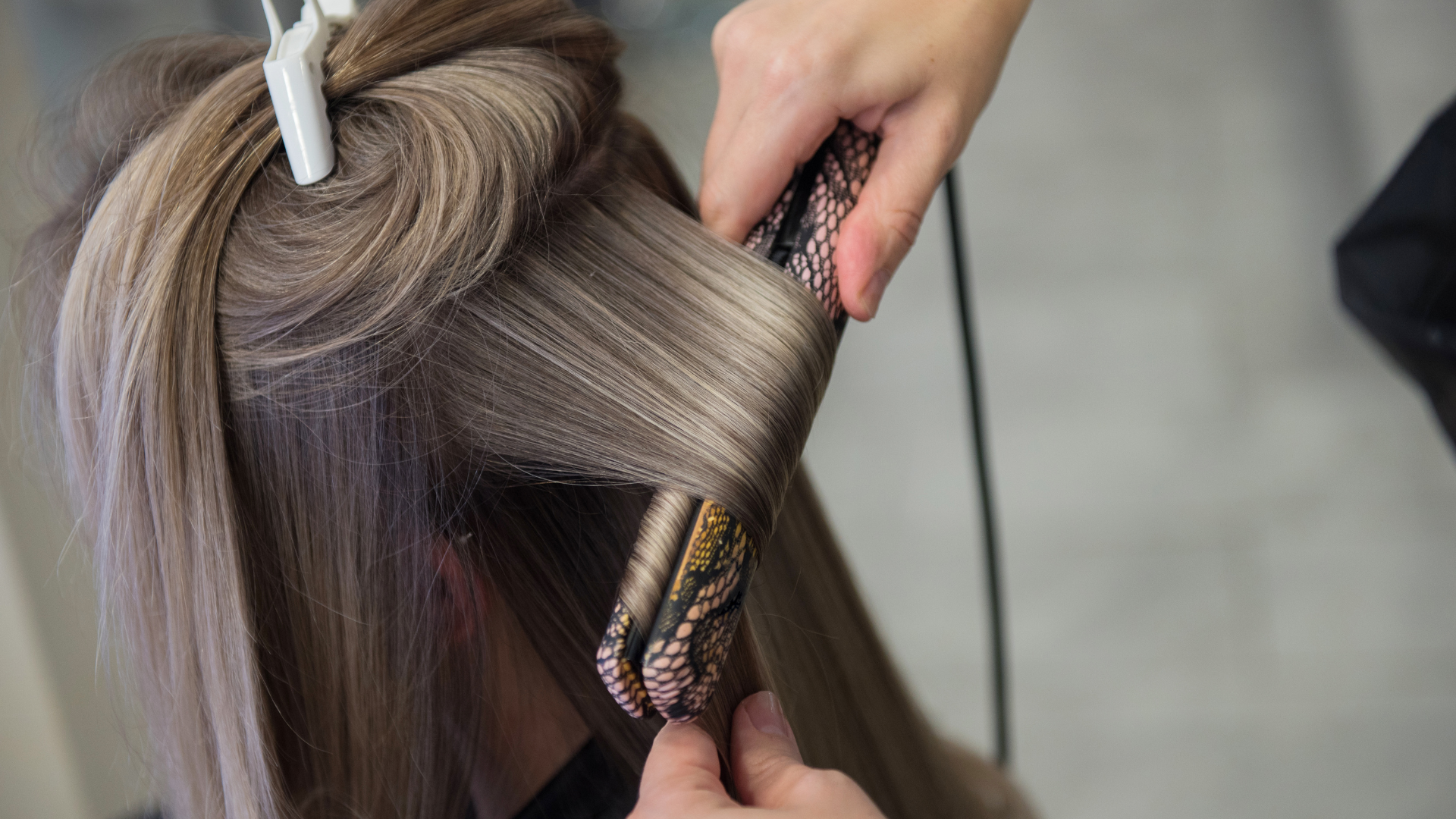 A person's hair being styled with a curling iron by a stylist.